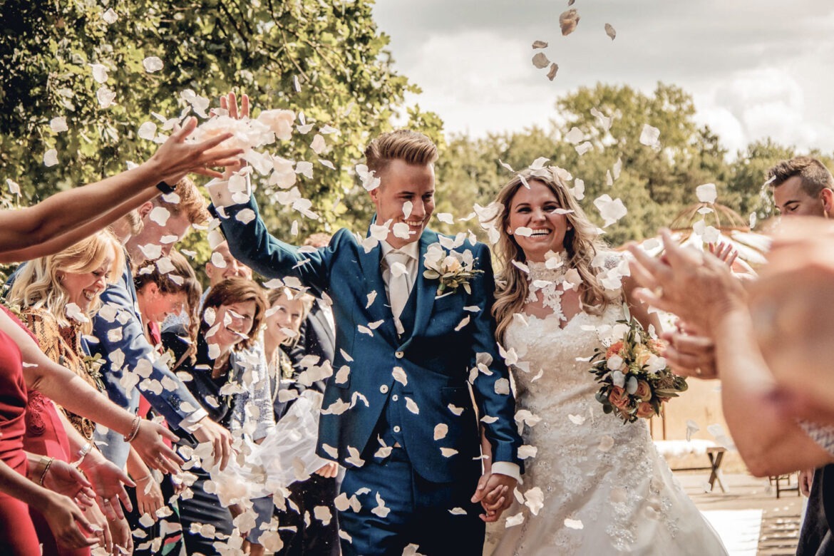 Bruidspaar wordt met rozenblaadjes bestrooid na een mooie trouwceremonie. Vastegelegd door de bruidsfotograaf van Trouwdag in Beeld